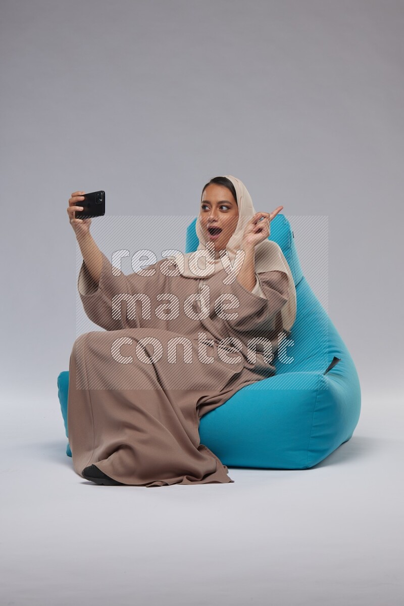 A Saudi woman sitting on a blue beanbag and taking selfie