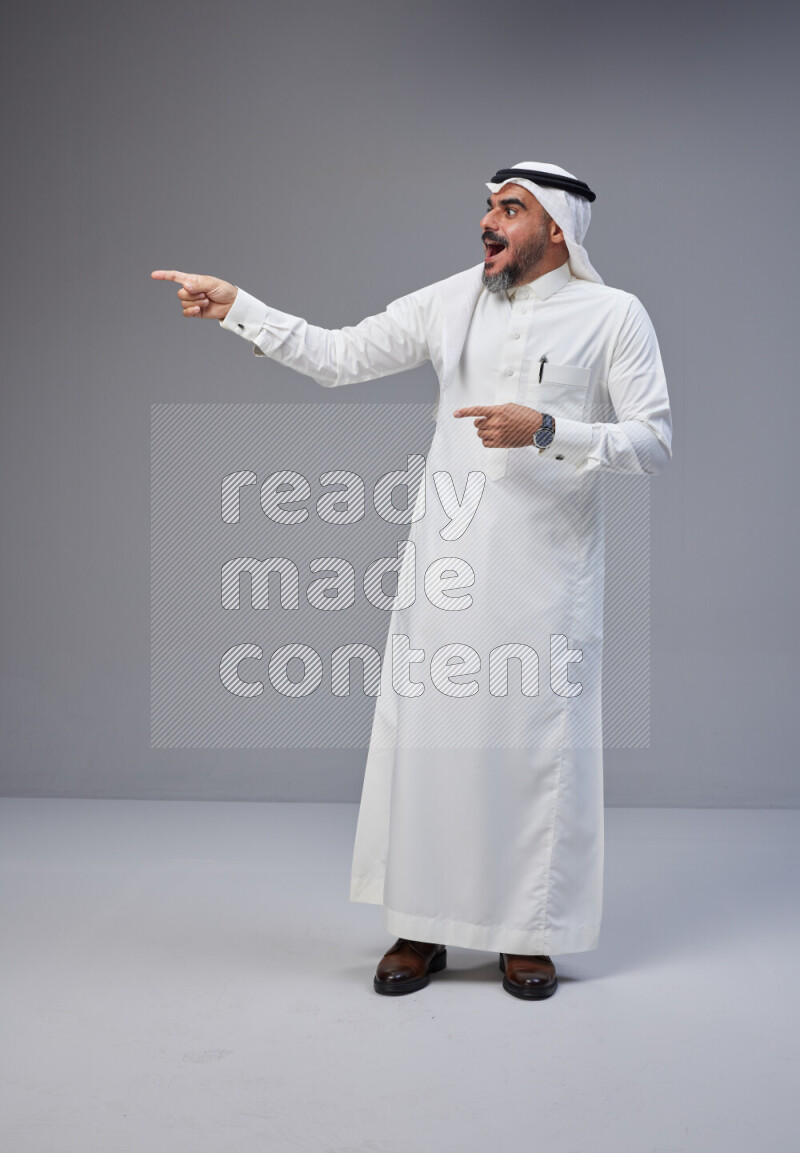 Saudi man Wearing Thob and white Shomag standing interacting with the camera on Gray background