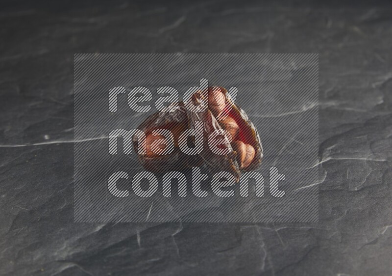 two hazelnuts stuffed madjoul dates on a black textured background
