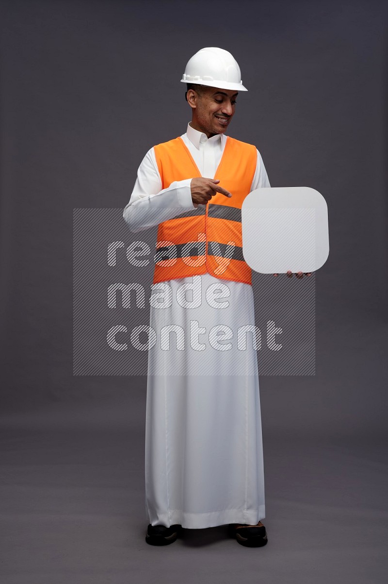 Saudi man wearing thob with engineer vest standing holding social media sign on gray background
