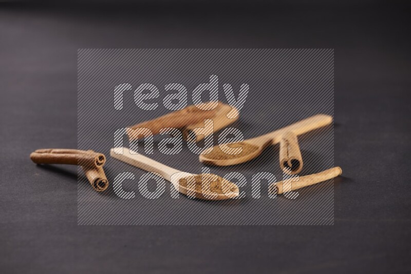 Two wooden spoons full of cinnamon powder with cinnamon sticks on black background