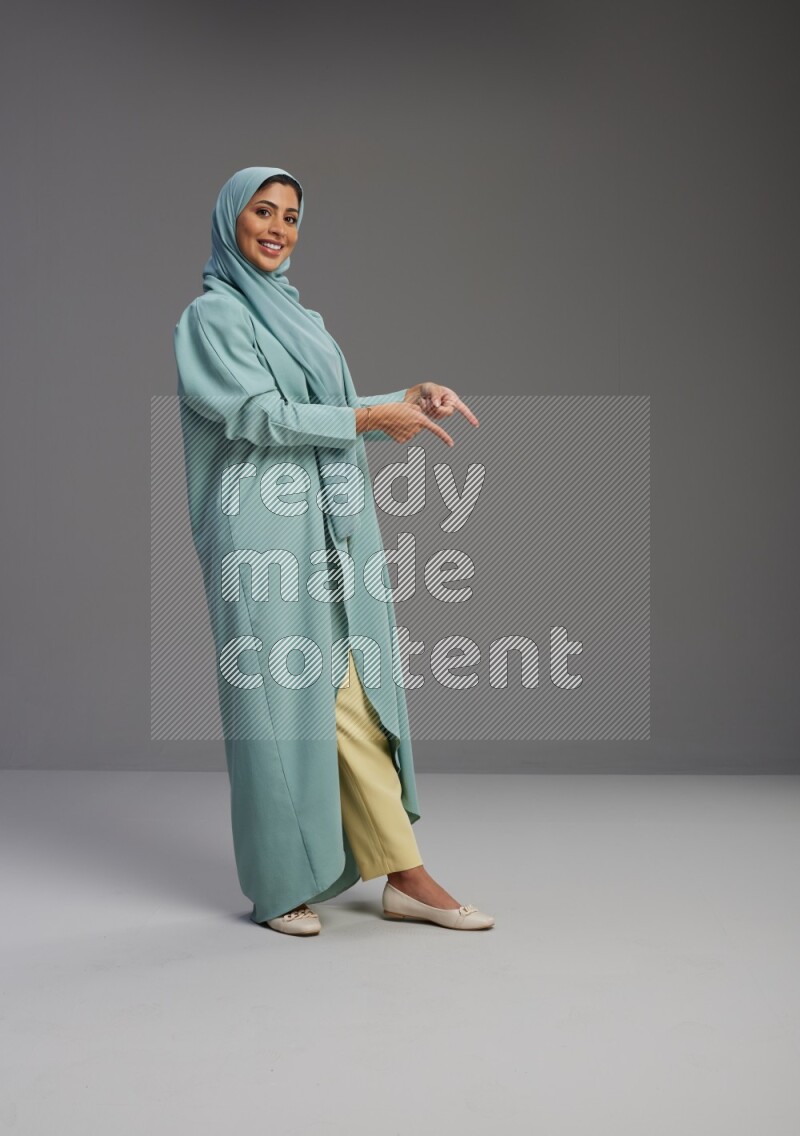 Saudi Woman wearing Abaya standing interacting with the camera on Gray background
