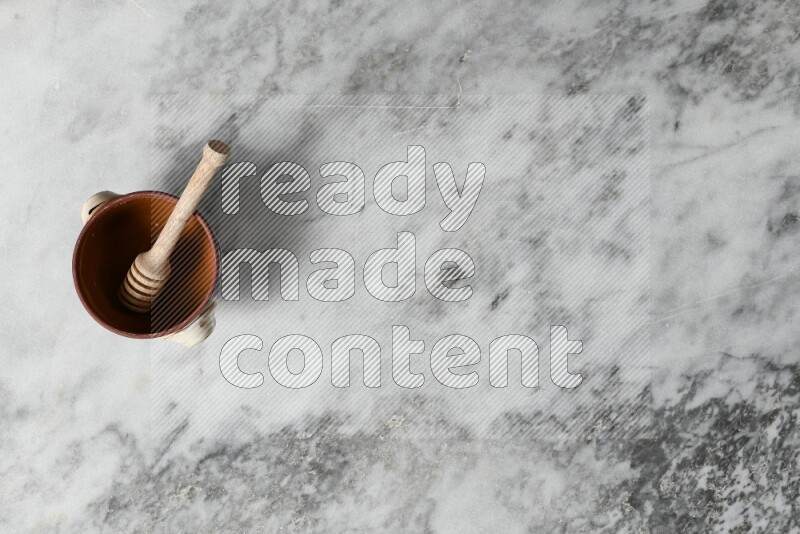 Decorative Pottery Pot with wooden honey handle in it, on grey marble flooring, Top View