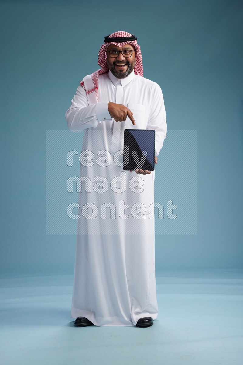 Saudi Man with shimag Standing holding a tablet on blue background