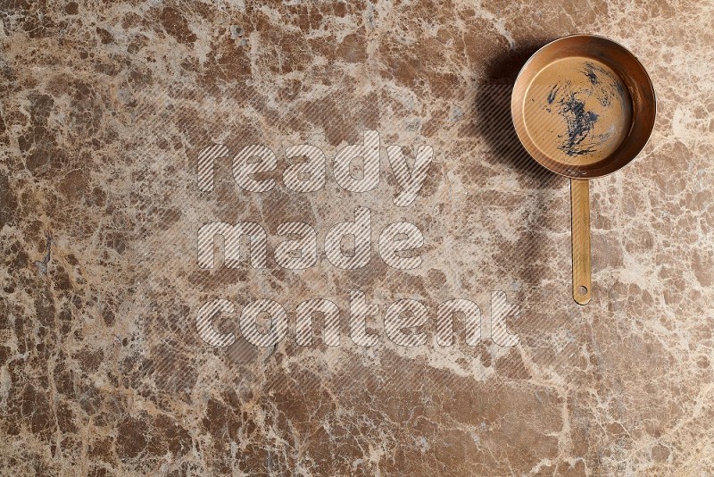 Top View Shot Of A Small Copper pan On beige Marble Flooring