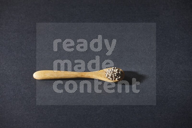 A wooden spoon full of white pepper beads on black flooring