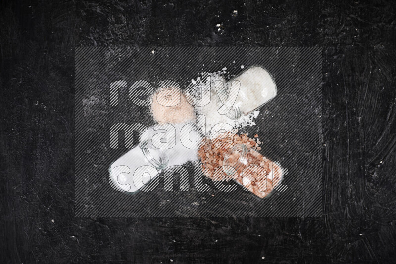 4 glass jars filled with table salt, coarse sea salt, fine himalayan salt and coarse himalayan salt on black background