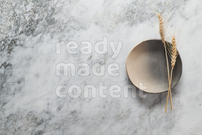 Wheat stalks on multicolored pottery plate on grey marble background