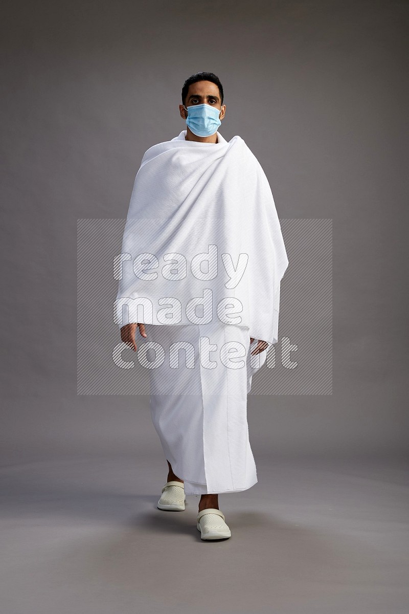 A man wearing Ehram with face mask Standing Interacting with the camera on gray background
