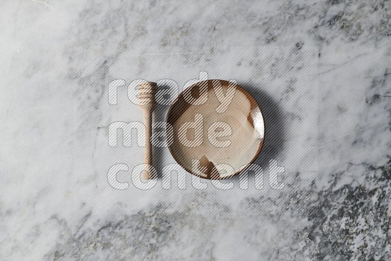 Multicolored Pottery Plate with wooden honey handle on the side on grey marble flooring, Top view