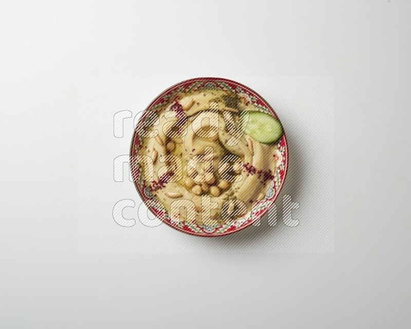 Hummus in a red plate with patterns garnished with zaatar & sumak on a white background
