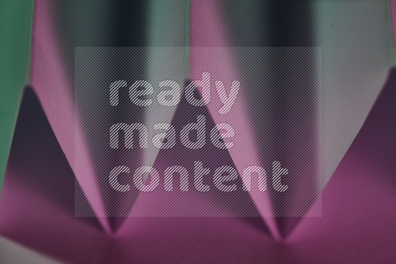 صورة مجردة مقربة تظهر طيات ورقية هندسية حادة بتدرجات اللون الأخضر والوردي