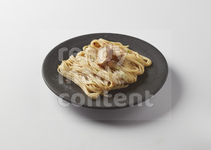spaghetti pasta with white sauce on a black plate on a white background