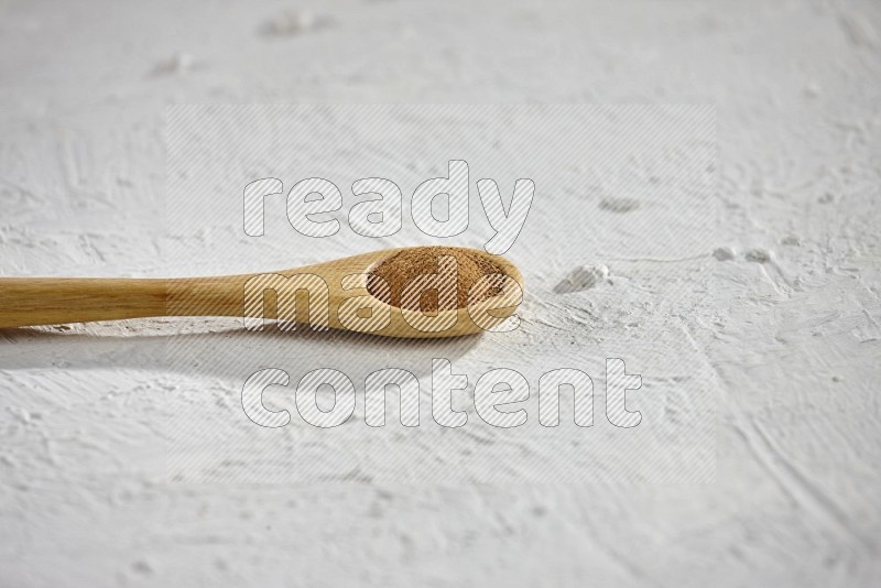 بودرة القرفة في ملعقة خشبية على خلفية بيضاء