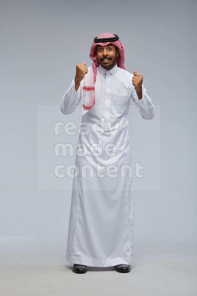Saudi man Wearing Thob and shomag standing interacting with the camera on Gray background