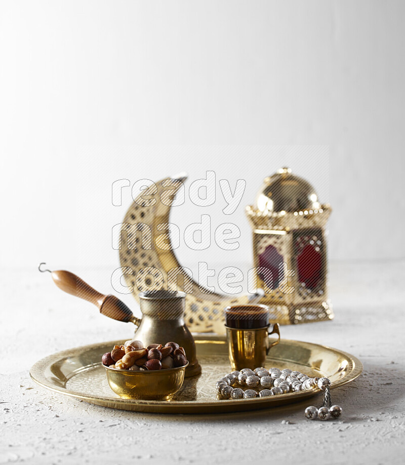 Nuts in a metal bowl with coffee and prayer beads on a tray beside lanterns in a light setup