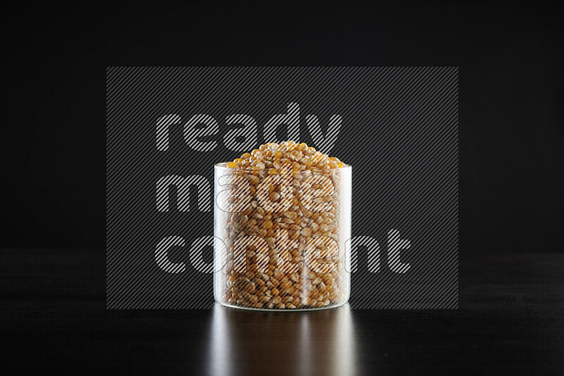Dry corn kernels in a glass jar on black background