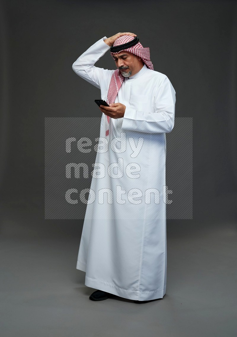 Saudi man with shomag Standing texting on phone on gray background
