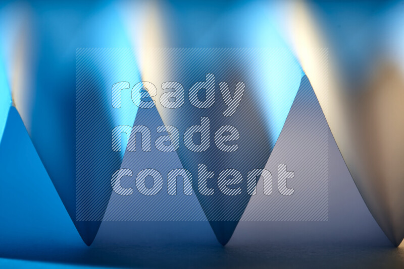 صورة مجردة مقربة تظهر طيات ورقية هندسية حادة بتدرجات اللون الأزرق مع درجات لونية دافئة