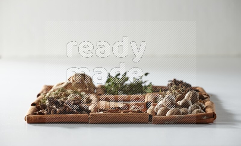 9 مربعات من أعواد القرفة، المربع الأوسط فارغ ومحاط بالنعناع المجفف والزنجبيل المجفف والهيل واليانسون والقرفة وجوزة الطيب والريحان المجفف والقرنفل على أرضية بيضاء