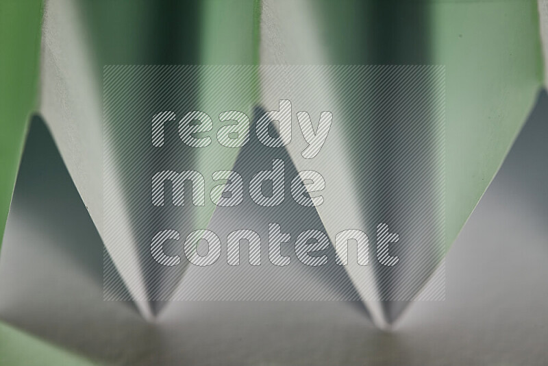 A close-up abstract image showing sharp geometric paper folds in white and green gradients