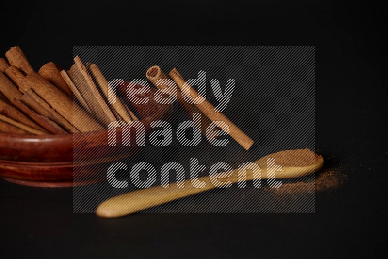أعواد القرفة في وعاء خشبي وبودرة القرفة في ملعقة خشبية على خلفية سوداء