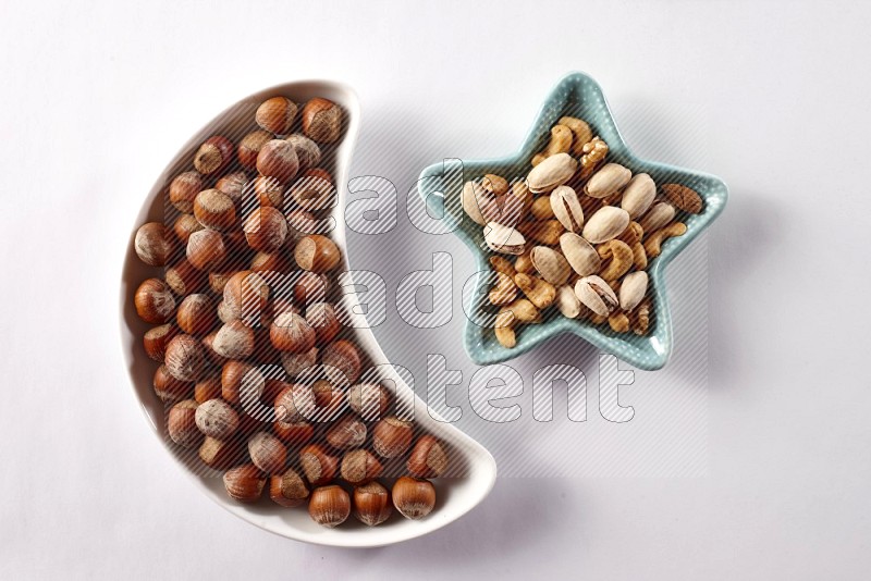 Hazelnuts in a crescent pottery plate and a star shaped plate with mixed nuts on white background