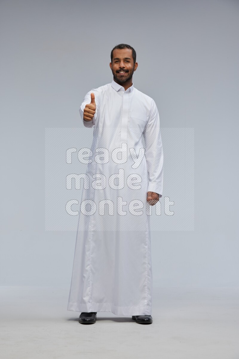 Saudi man Wearing Thob standing interacting with the camera on Gray background