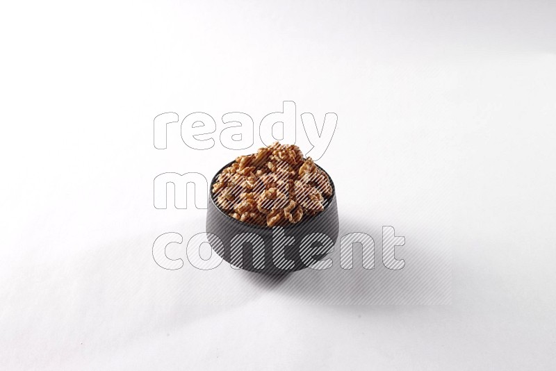 Walnuts in a black pottery bowl on white background