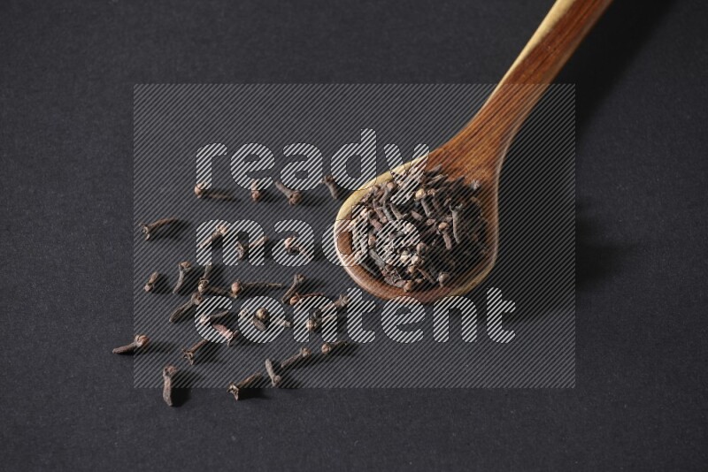 A wooden ladle full of whole cloves on a black flooring