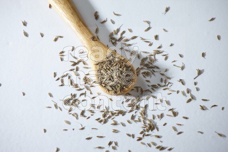 A wooden spoon full of cumin seeds on a white flooring