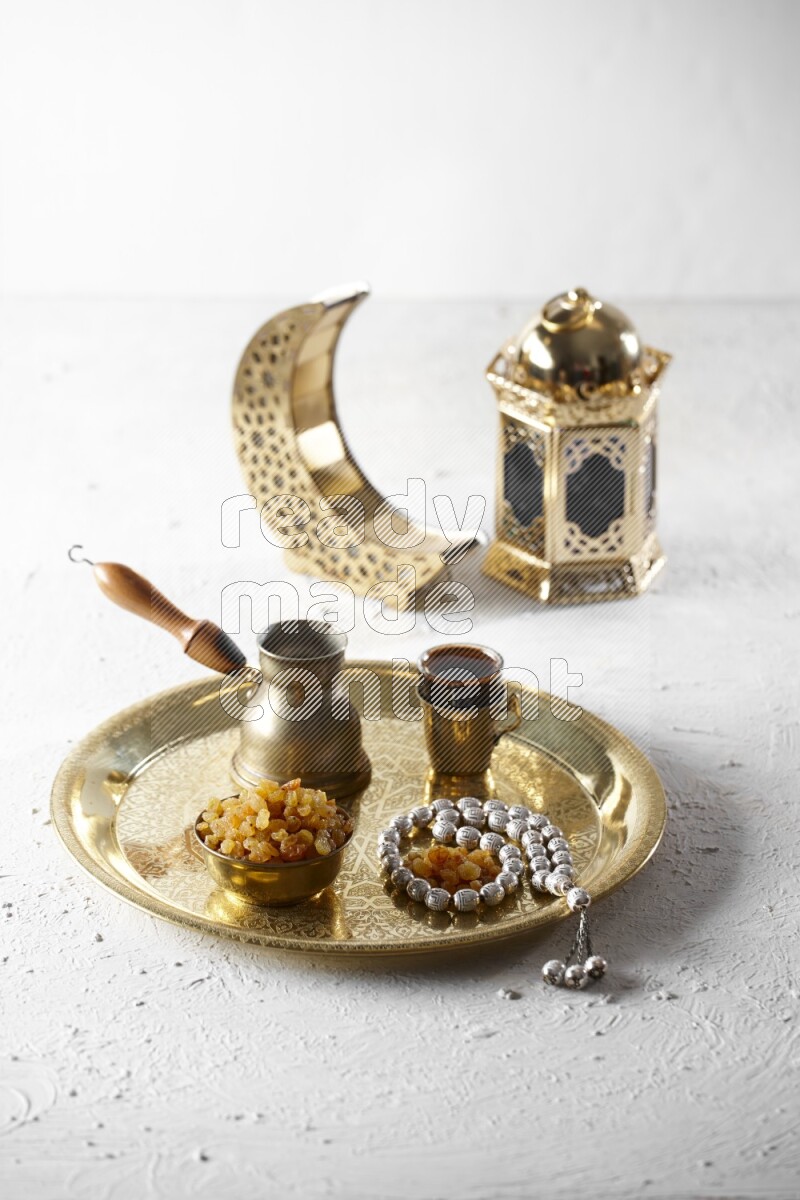 زبيب في وعاء معدني مع قهوة وسبحة على صينية بجانب فوانيس علي خلفية بيضاء