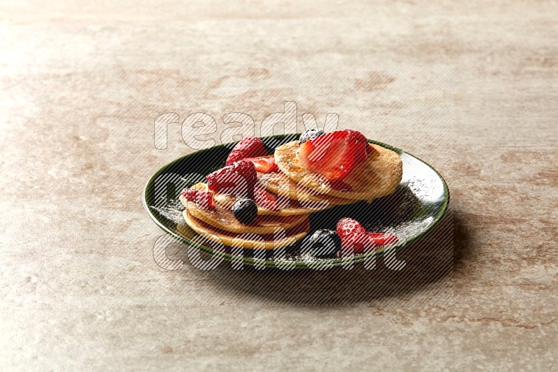 Five stacked mixed berries mini pancakes in a green plate on beige background