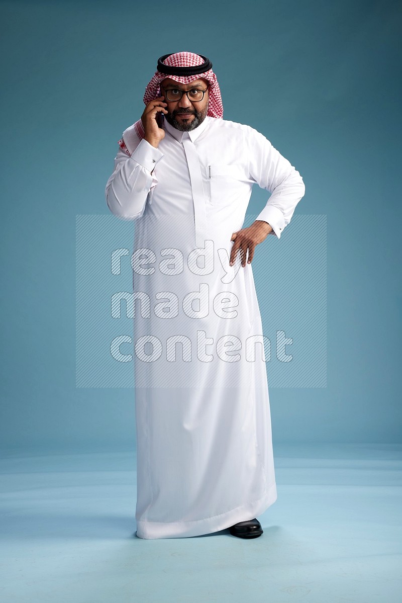 Saudi Man with shimag Standing talking on phone on blue background
