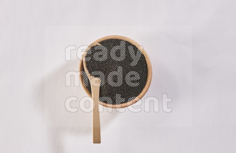 وعاء خشبي وملعقة خشبية كلاهما ممتلئ ببذور حبة البركة علي خلفية بيضاء