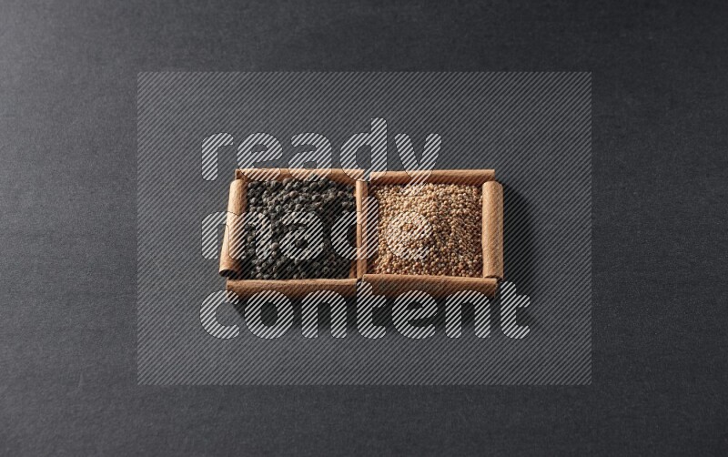 مربعان من أعواد القرفة ممتلئان بحبوب الخردل وحبوب الفلفل الأسود علي خلفية سوداء