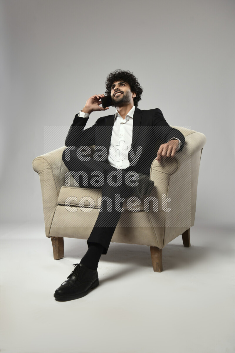 A man wearing formal sitting on a chair talking on the phone on white background