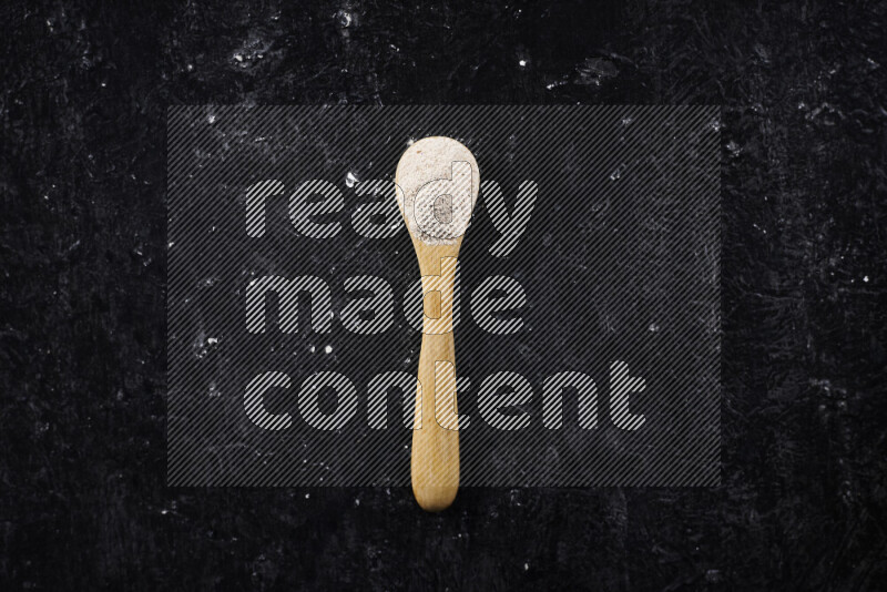 A wooden spoon full of onion powder on black background