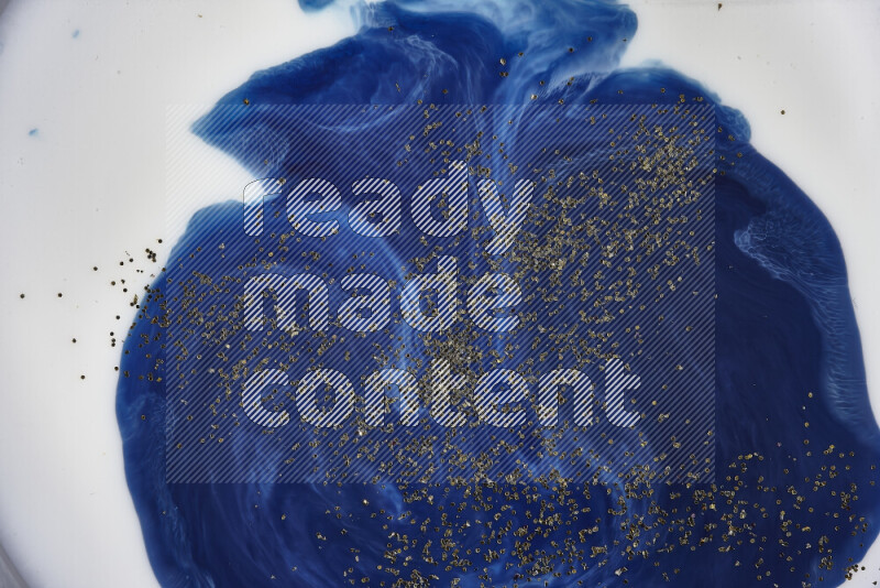 A close-up of sparkling gold glitter scattered on swirling blue background