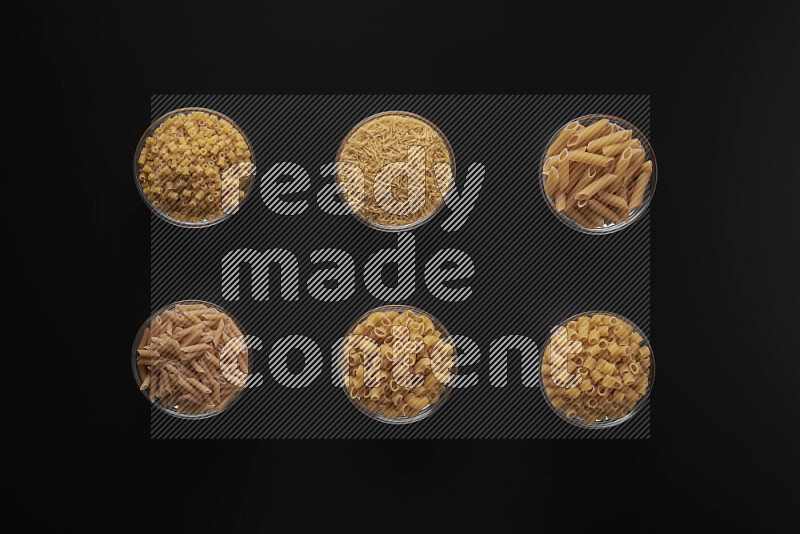 Different pasta types in 6 glass bowls on black background