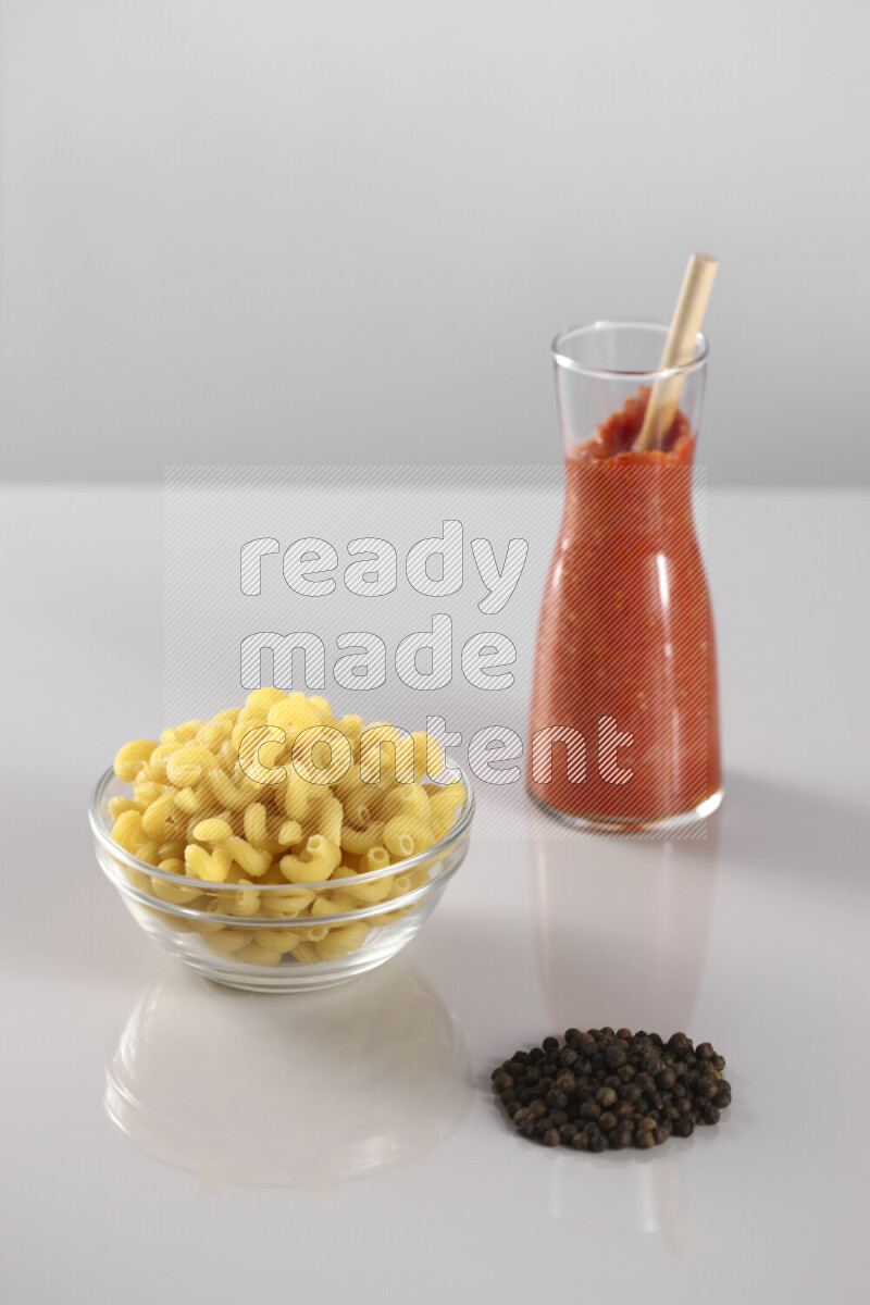Raw pasta with tomatoe pasta with different ingredients such as cherry tomatoes, basil, garlic, bay laurel, cardamom, white pepper, black pepper, red chilis and wheat stalks on light grey background