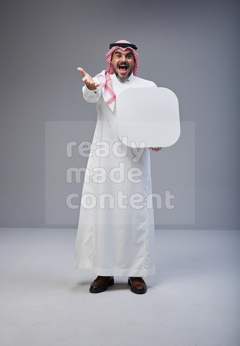 Saudi man Wearing Thob and red Shomag standing holding social media sign on Gray background