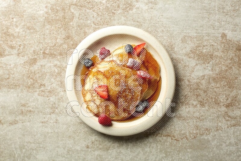 Three stacked mixed berries pancakes in a grey plate on beige background
