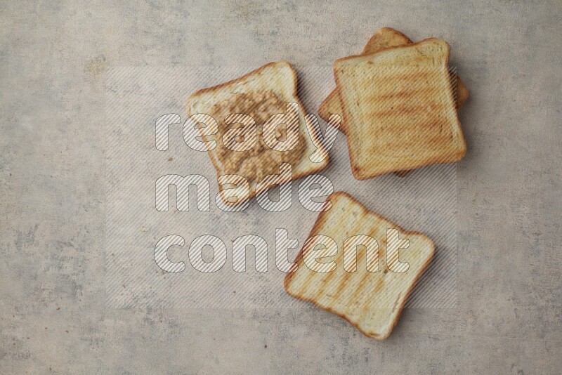 Crunchy peanut butter on a toasted white toast and toasted white toast slices on a light blue textured background