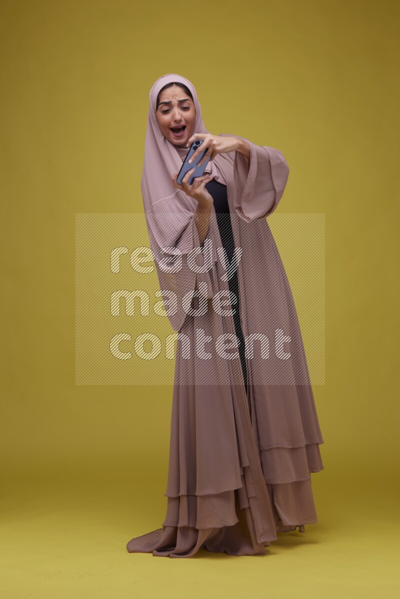 A woman Playing Games a Yellow Background wearing Brown Abaya with Hijab