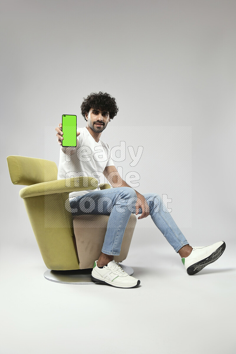 A man wearing casual sitting on a chair showing a phone screen on white background