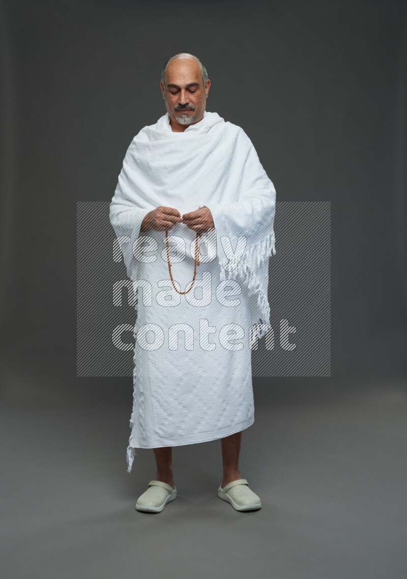 A man wearing Ehram Standing holding rosary on gray background