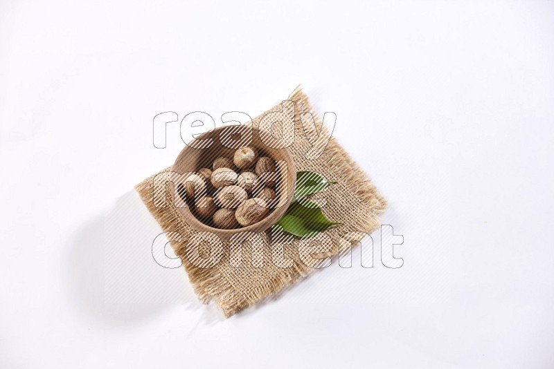 A wooden bowl full of nutmeg on burlap fabric on a white flooring in different angles