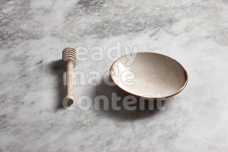 Multicolored pottery plate with wooden honey dipper on the side on grey marble background