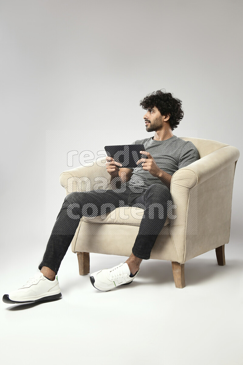 A man wearing casual sitting on a chair gaming on a tablet on white background